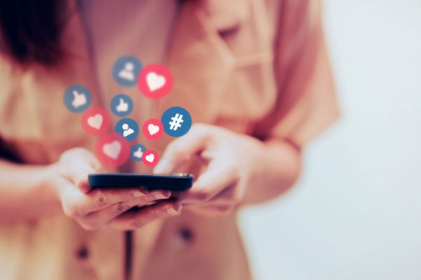 social-media-frau Frau hält Smartphone in der Hand, Icons für Likes, Hashtags, Personen kommen aus dem Display