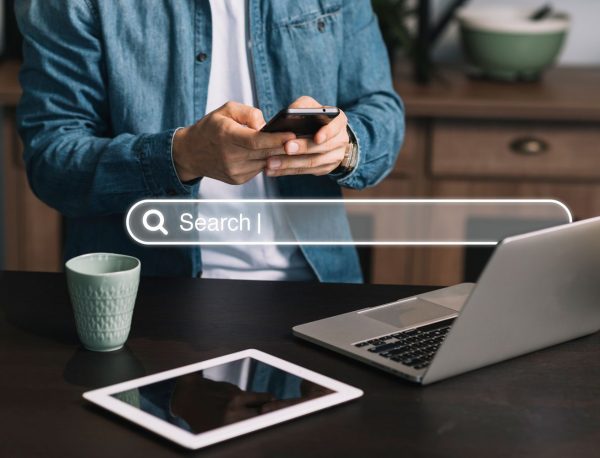 seo Mann mit Smartphone in der Hand. Suchmaske für Suchmaschinen erscheit in weiß über dem Bild.